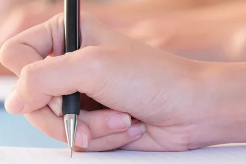 Mão escrevendo com lapiseira numa folha